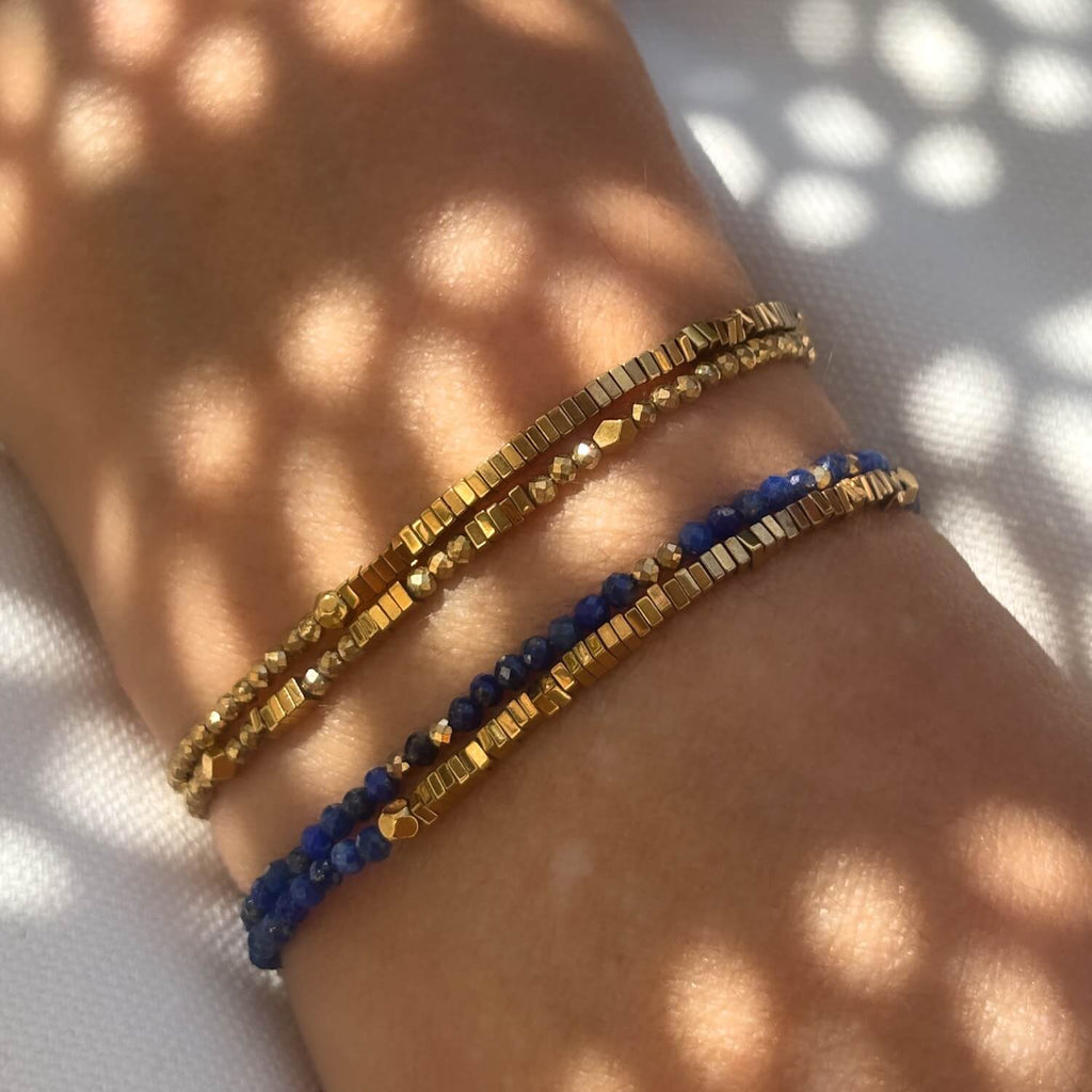 Gold and blue beaded bracelets on a wrist with a sunlit background