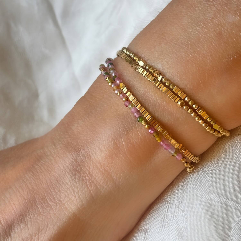 Close up of  2 Golden Hematite  and Tourmaline wrap double strand gemstone bracelets on a models arm against white background