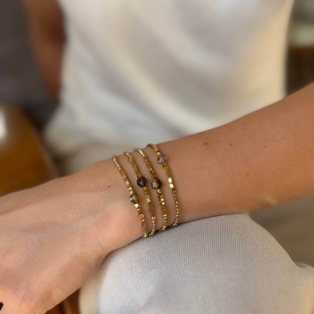 Close-up of a wrist wearing multiple golden gemstone beaded bracelets on a neutral background
