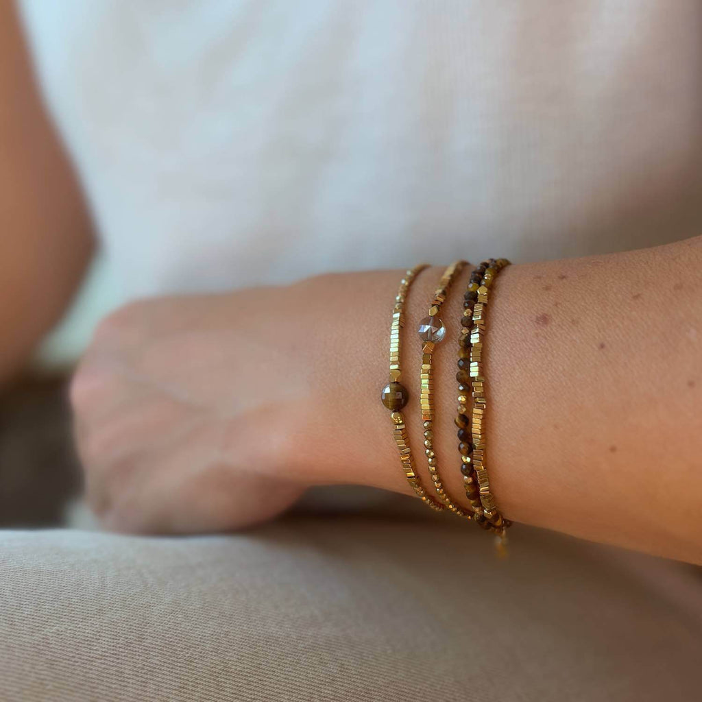 Close-up of a wrist wearing 3 beaded gemstone bracelets on a neutral background