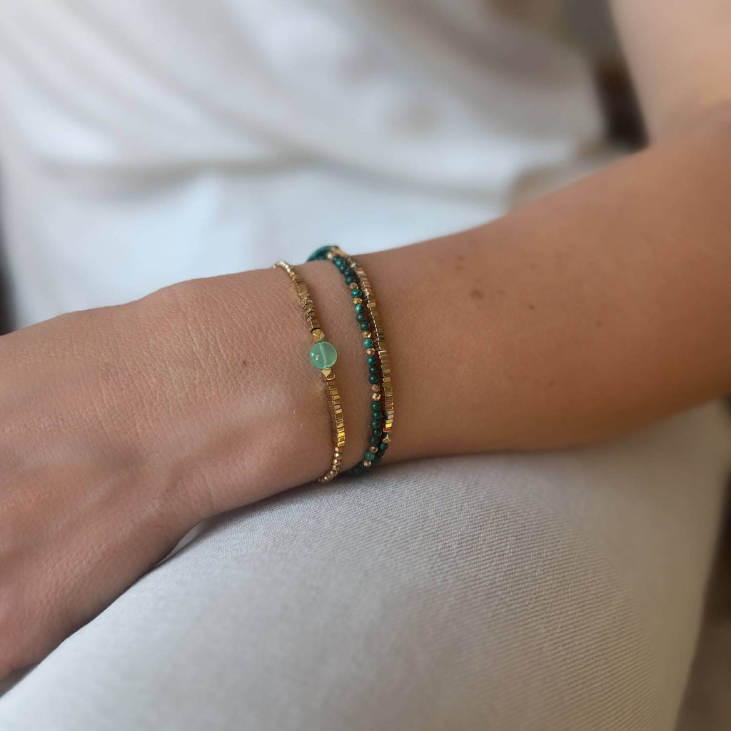 Close-up of a wrist wearing two Green gemstone bracelets on a neutral background