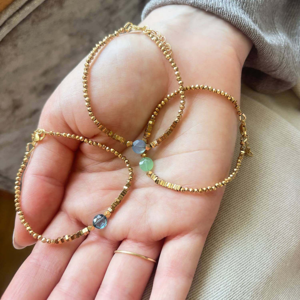 Close-up of a hand holding 3 elegant golden Hematite beaded bracelets with a colourful central gemstone