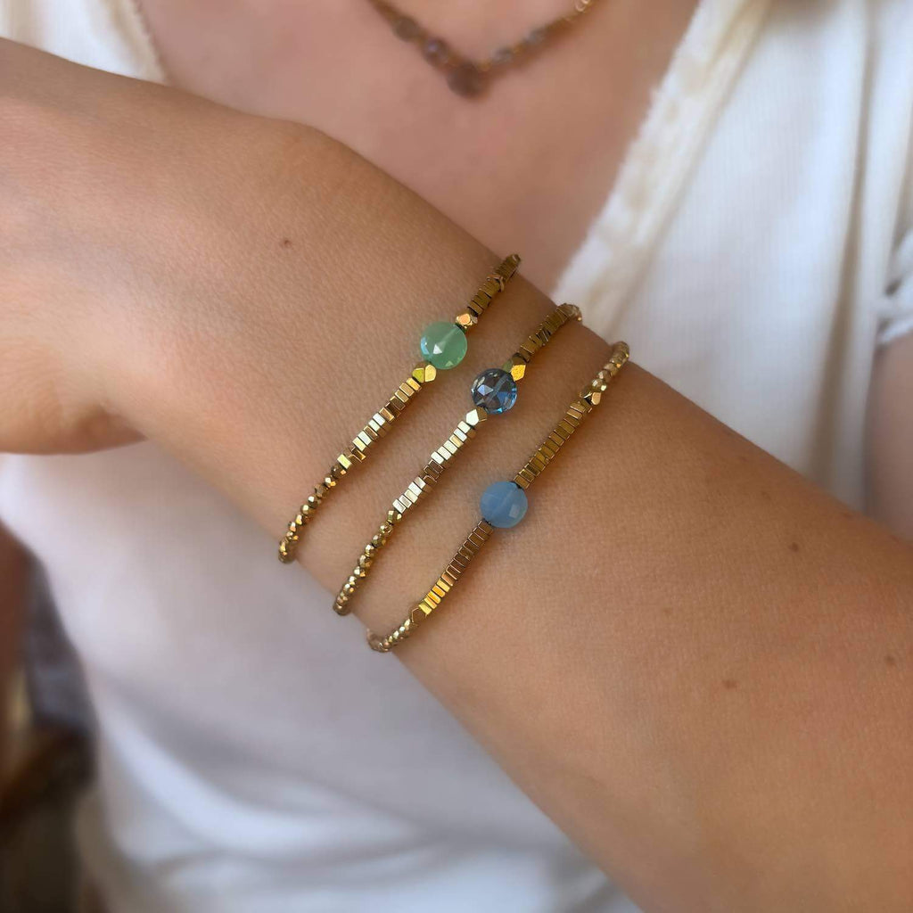 Close-up of a wrist wearing three blue and green gemstones beaded bracelets with gemstones on a blurred background.