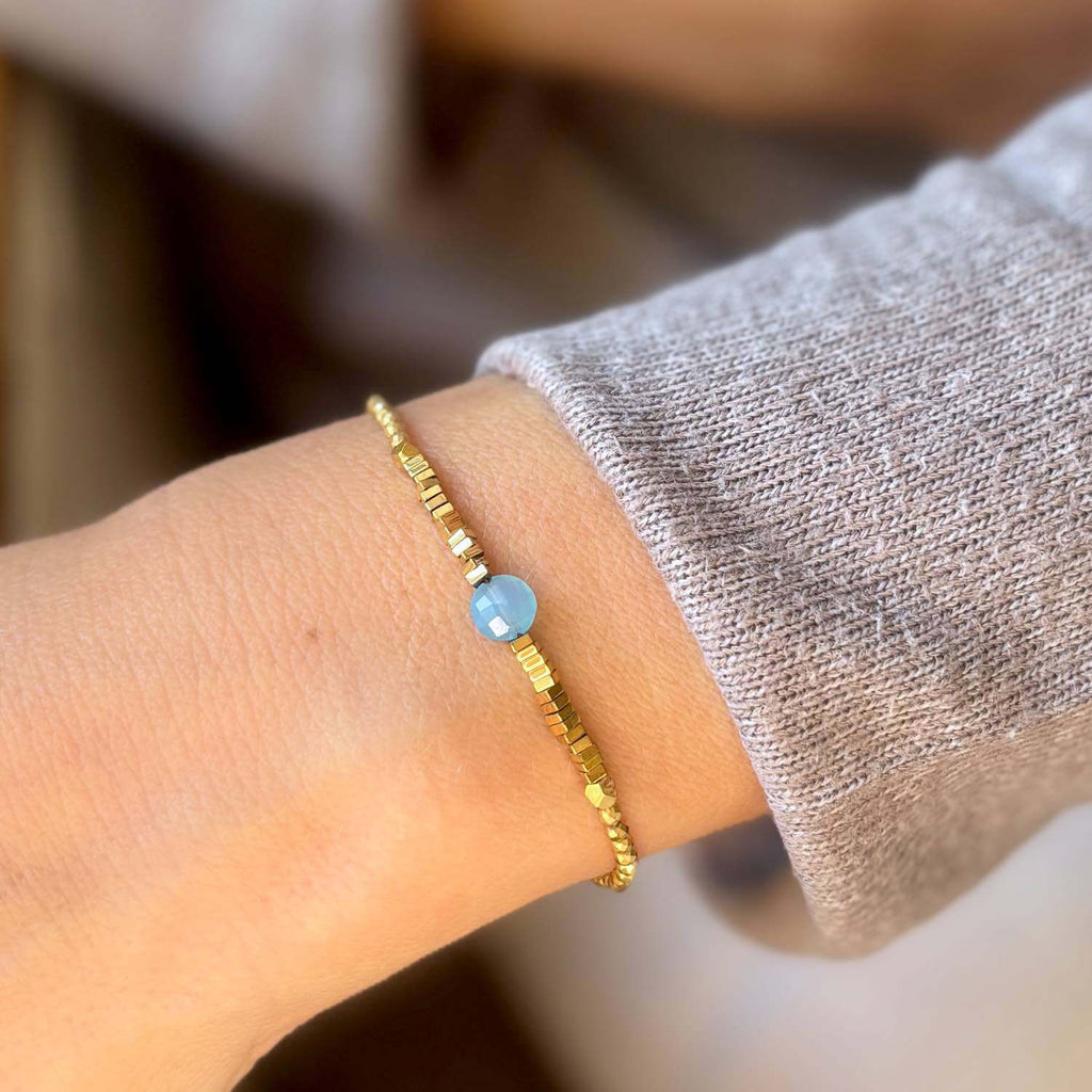 Gold en hematite bracelet with a blue quartz gemstone on a wrist against a blurred background