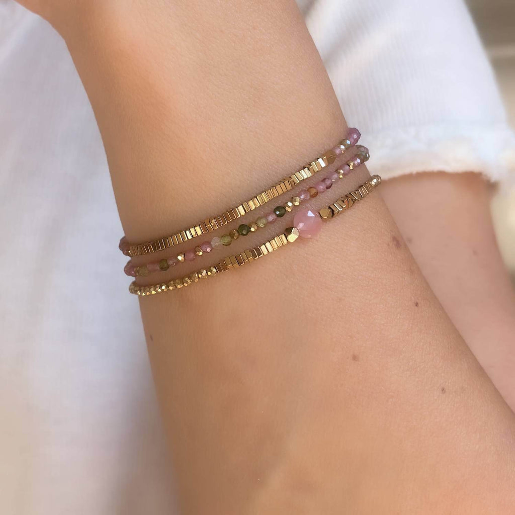 Close-up of a wrist wearing two beaded Pink Quartz and tourmaline gemstone bracelets on a blurred background 