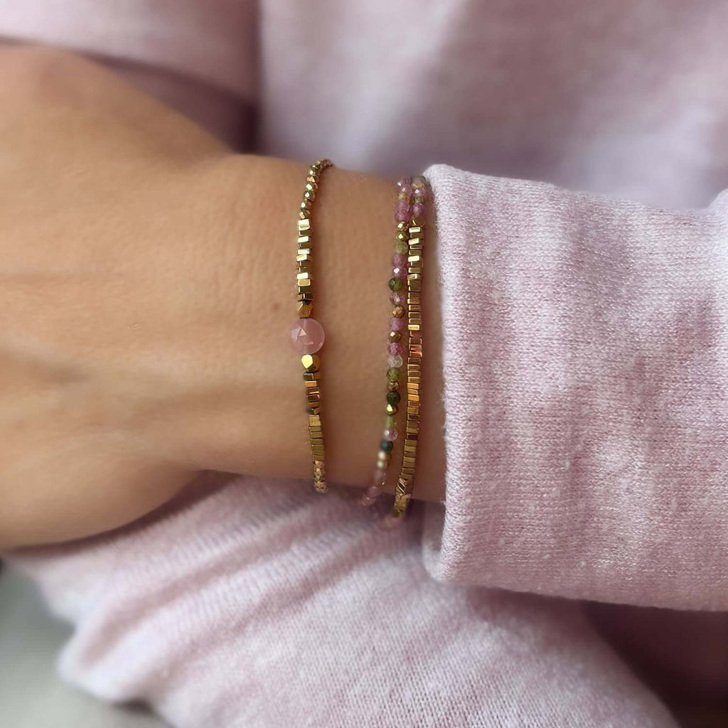 Close-up of a wrist wearing two beaded Pink Quartz and tourmaline gemstone bracelets on a light pink fabric background 