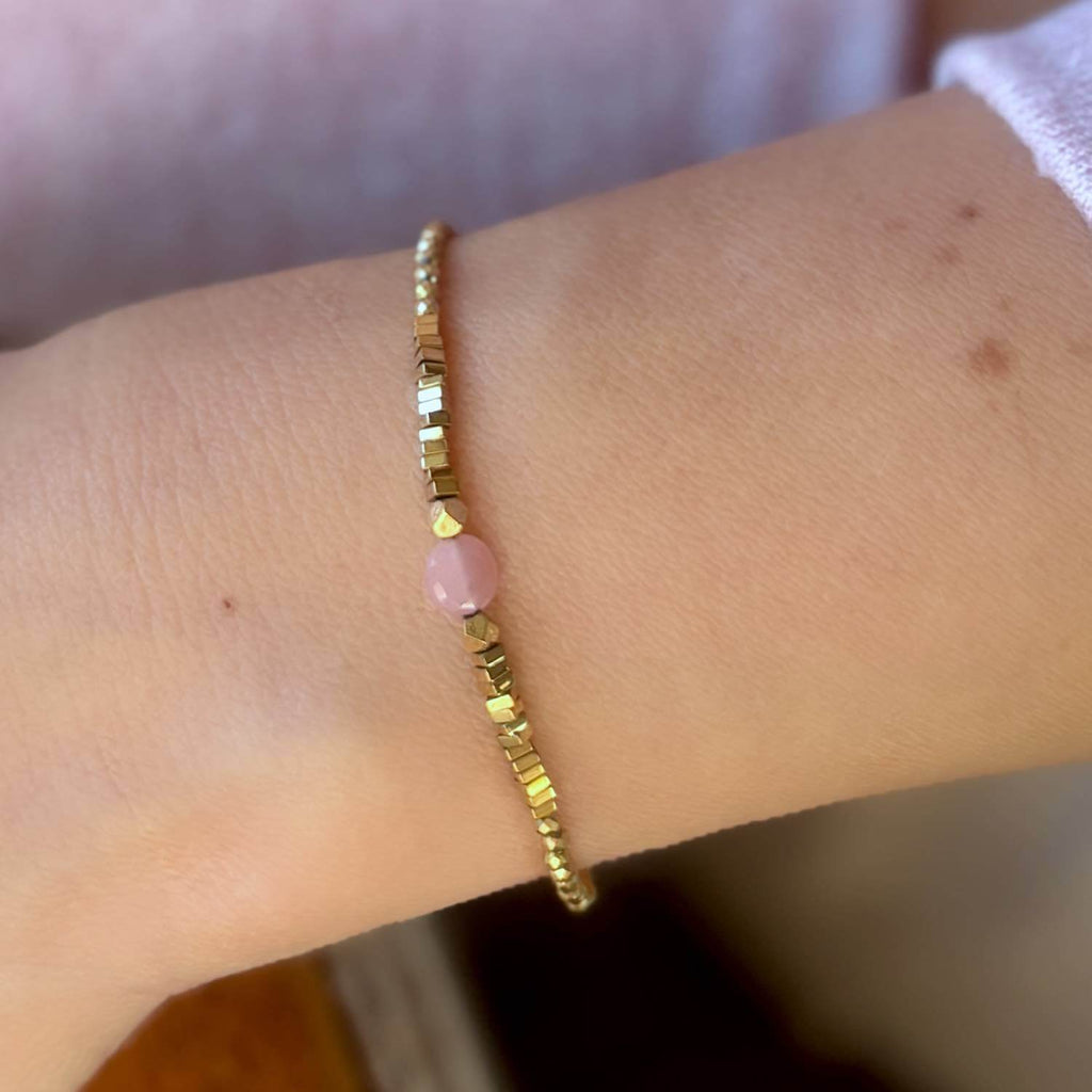 Gold Hematite bracelet with a pink guava quartz gemstone bead on a wrist against a blurred background