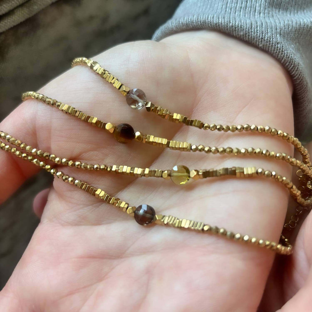 Close-up of a hand holding 3 elegant golden Hematite beaded bracelets with golden brown central gemstones