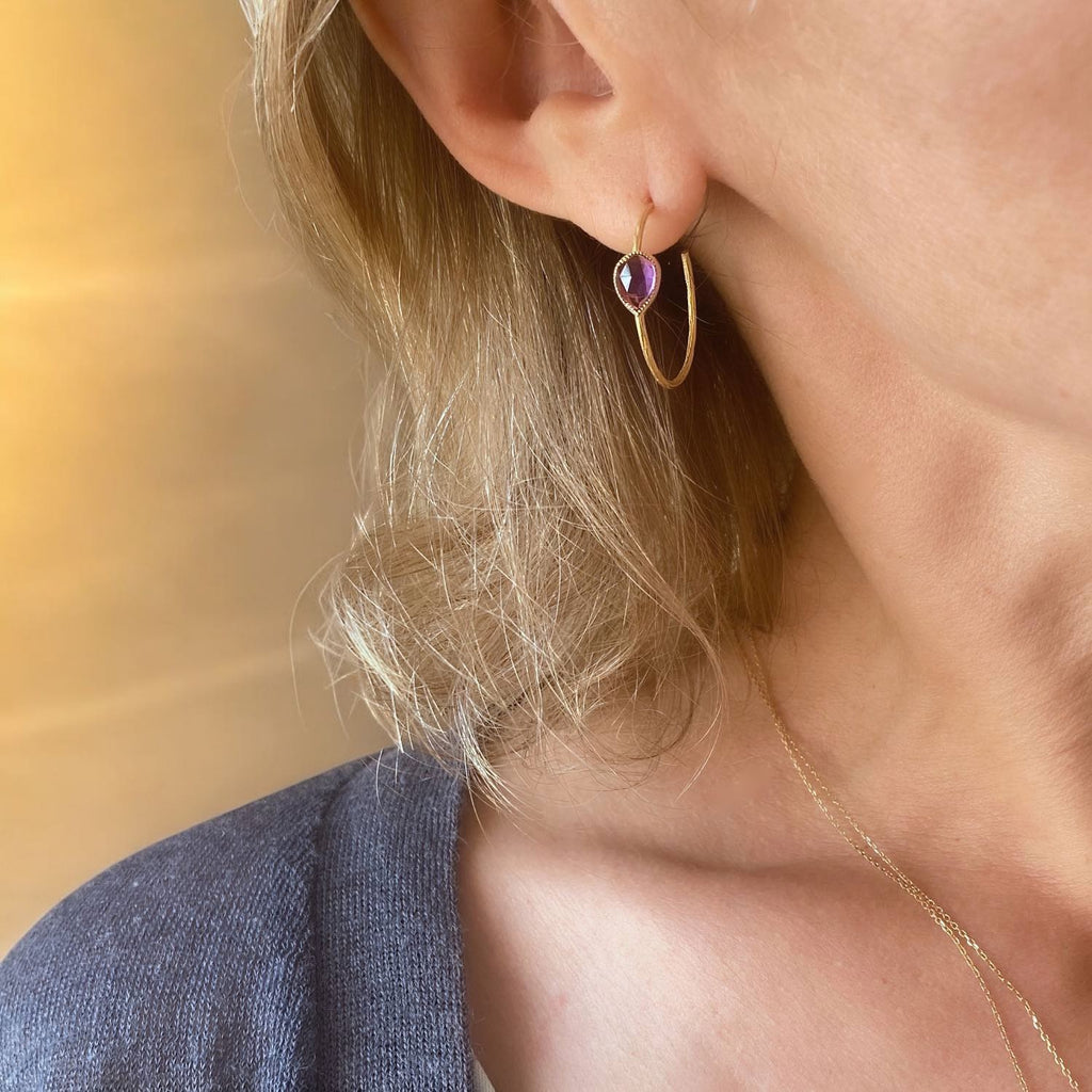 model wearing large hoop earrings in 18k gold and faceted drop shape amethyst gemstone