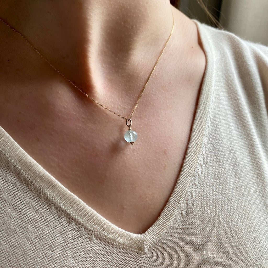 Aquamarine pendant or charm in 18k Gold, faceted button gemstone on a gold chain on a model, beautiful natural blue milky colour