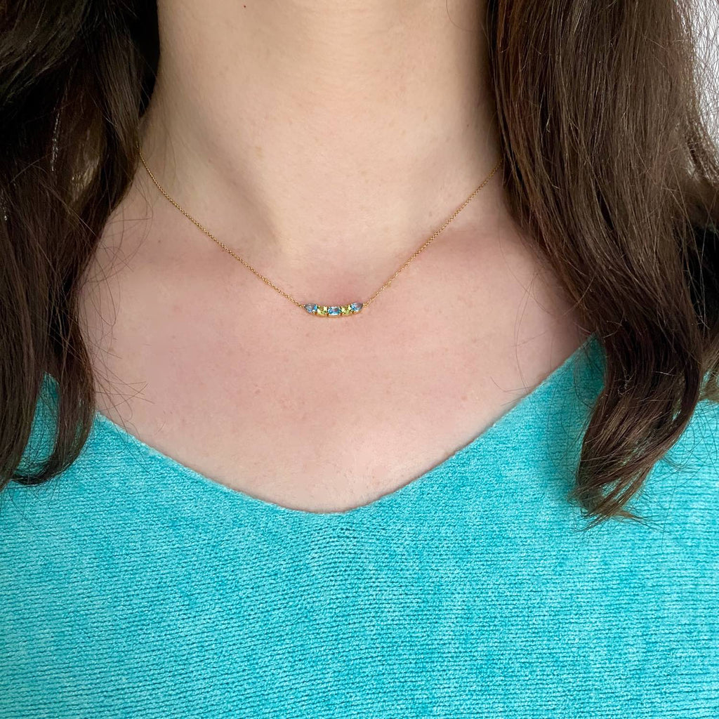 A luminous and unique 18k gold choker necklace with a central curved bar pattern of Swiss Blue Topaz and Peridot set on claws, displayed on a model’s neck.