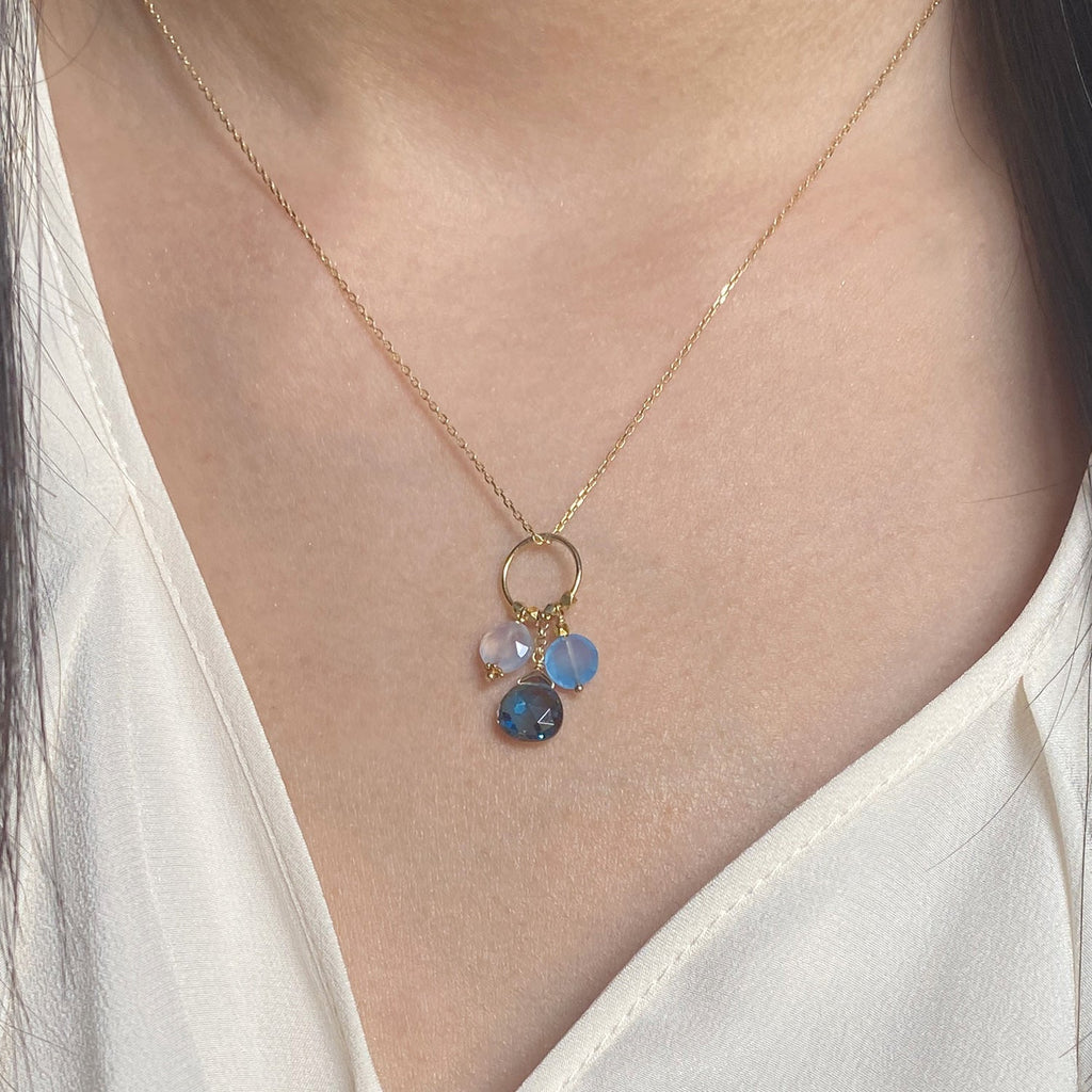 A 18k chain with a charm with 3 gemstones of Blue Chalcedony, Blue Topaz, Blue Quartz  hanging on a ring displayed on a model neck