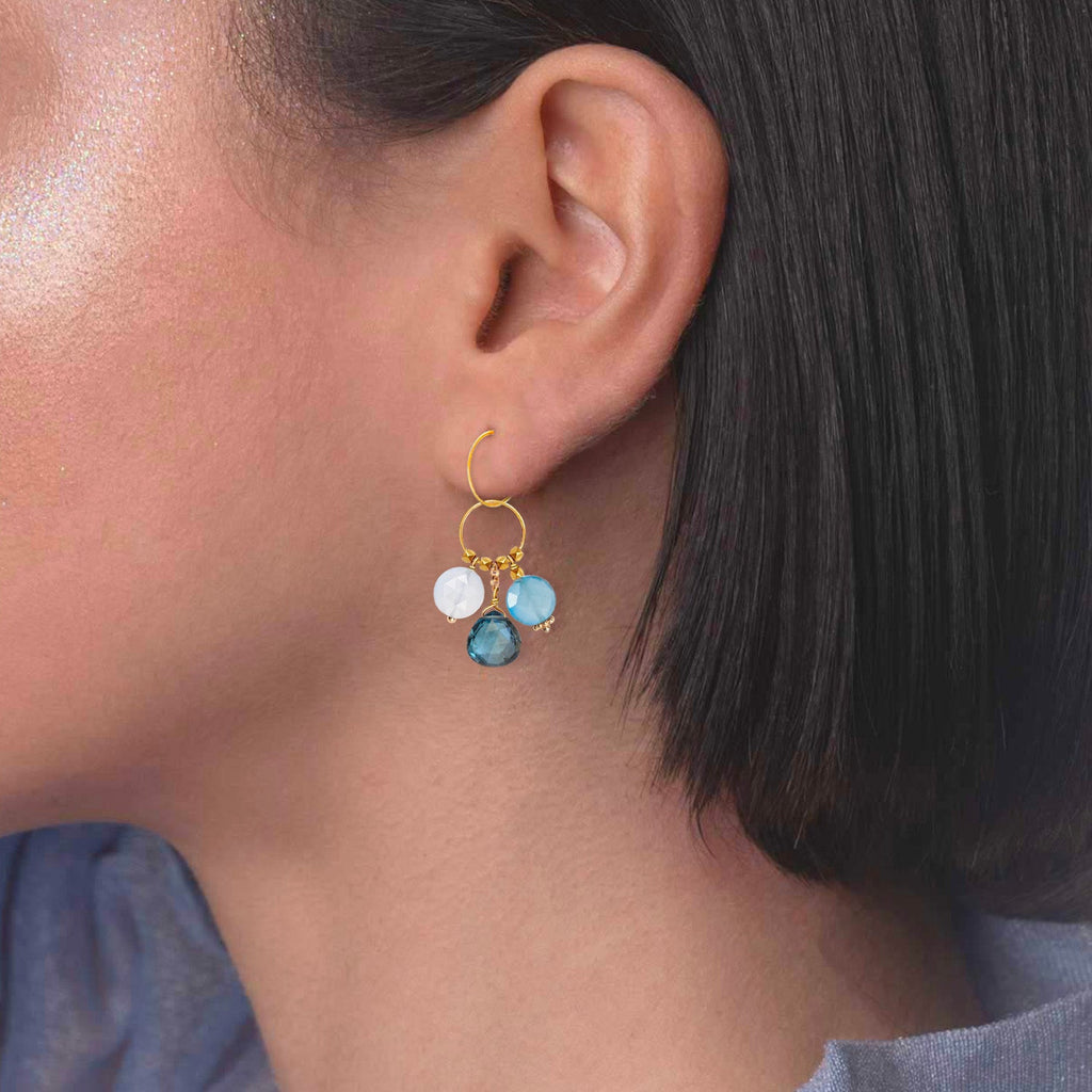 A gemstone charm in 18k gold with a trio of of Blue Chalcedony, Blue Topaz, Blue Quartz   on a model ear 