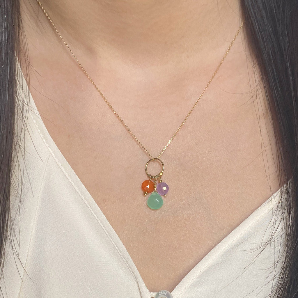 A 18k chain with a charm with 3 gemstones of Carnelian, Chrysoprase & Lavender Jade hanging on a ring displayed on a model neck