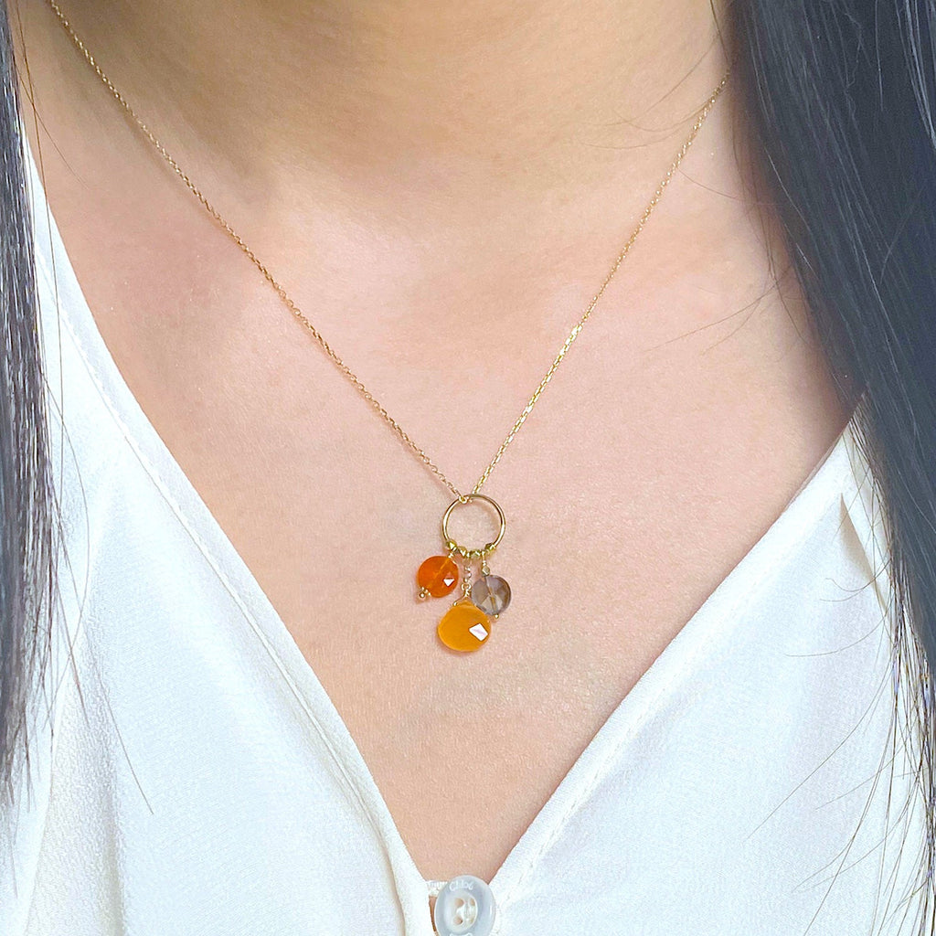 A 18k chain with a charm with 3 gemstones of Carnelian, Orange Jade and  Smoky Quartz hanging on a ring displayed on a model neck