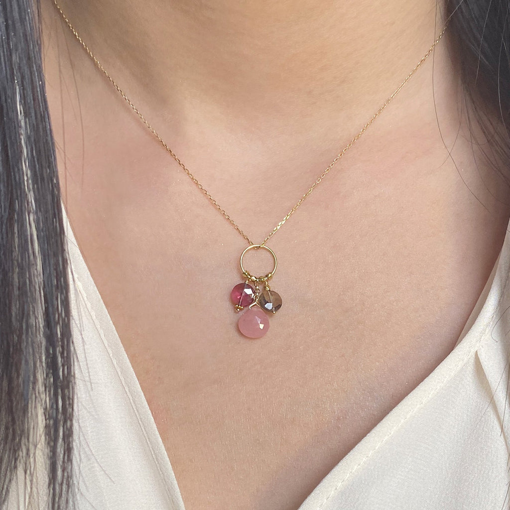 A 18k chain with a charm with 3 gemstones of Garnet, Guava Quartz & Smoky Quartz  hanging on a ring displayed on a model neck